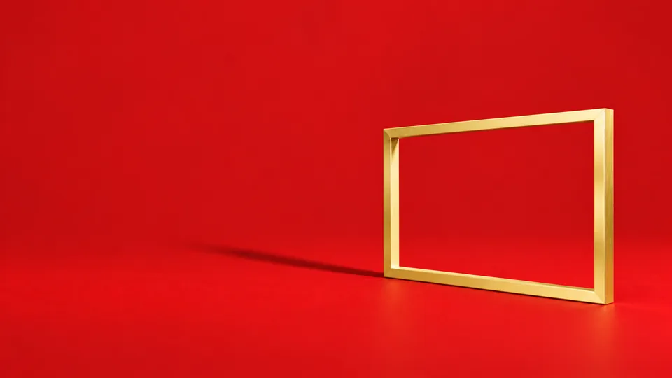 A simple pale-gold picture frame on a vermilion surface.